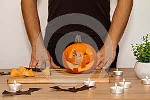 A man carves eyes and a mouth in a pumpkin for Halloween.