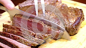 Man carves shank of roast beef steak on a wooden board. Seam comes out from hot beef flank.