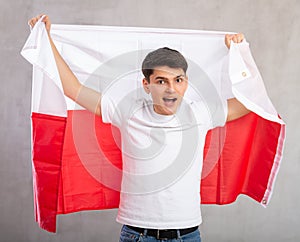 Man in casual clothes holds unfurled flag of Poland in hands raised above head photo
