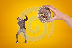 Man in casual clothes protecting himself from hand with a roulette on yellow background