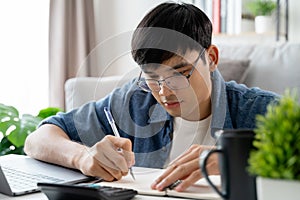 the man in casual clothes working with a laptop, computer, smart phone, calculator sitting on the sofa in the living room at home