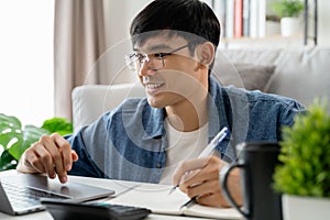 the man in casual clothes working with a laptop, computer, smart phone, calculator sitting on the sofa in the living room at home