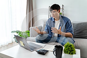 the man in casual clothes working with a laptop, computer, smart phone, calculator sitting on the sofa in the living room at home