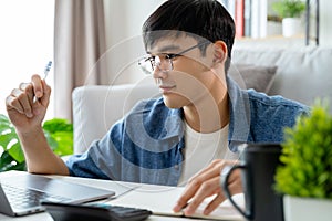 the man in casual clothes working with a laptop, computer, smart phone, calculator sitting on the sofa in the living room at home