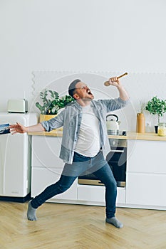 Man in casual clothing singing in spoon in kitchen dancing enjoying life