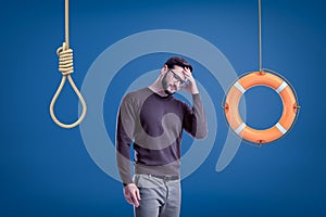 Man in casual outfit standing half-turn with hand on forehead as if choosing between lifebuoy hanging on rope and