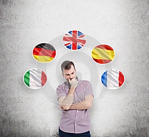 Man in casual shirt holds his chin and thinks about which language to study. Italian, German, United Kingdom, Spanish and Fr