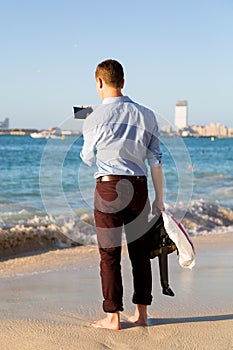 A man in casual wear on the beach with a phone.