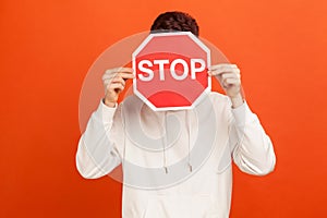 Man in casual white hoodie hiding behind stop sign, teenager afraid of bullying, victim of domestic violence