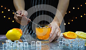 man catch glass, stir ice and orange near fresh slice lemon and orange