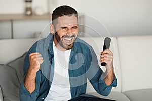 man celebrates football victory shouting with remote in hand indoors