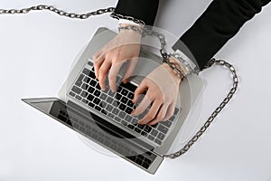 Man with chained hands typing on laptop against white background, top view. Internet addiction