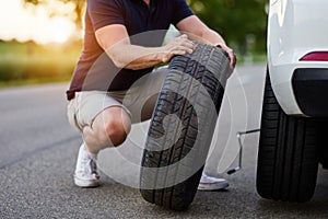 The man changes the tire to a broken car