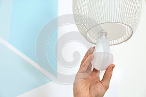 Man changing light bulb in lamp against color wall, closeup.