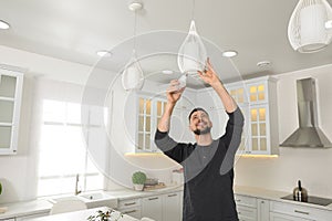 Man changing light bulb in lamp at home. Space for text photo