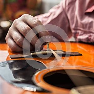 A man changing old ripped guitar strings on the acoustic guitar