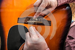 A man changing old ripped guitar strings on the acoustic guitar