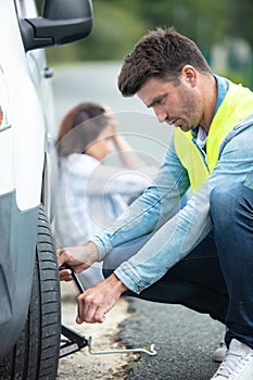 man changing tyre while woman upset