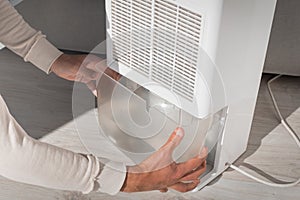 Man changing water container in air dryer, dehumidifier, humidity indicator. Humid air at home.