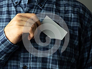 a man in a checked blue shirt tucks a business card into his pocket