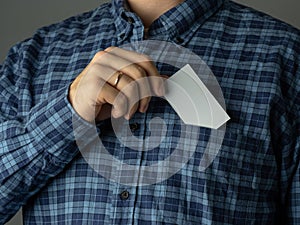 A man in a checked blue shirt tucks a business card into his pocket