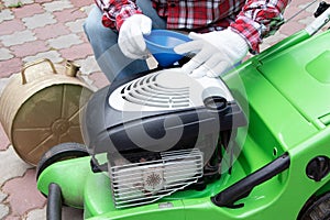 A man Checking the fuel level in lawn mower. A green lawnmower. Gardening. Maintenance of equipment