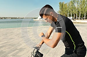 Man checking modern smart watch during training near river
