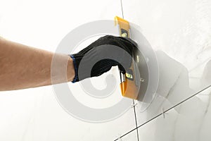 Man checking proper ceramic tile installation with level on wall, closeup.