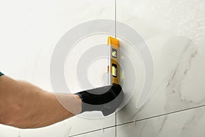 Man checking proper ceramic tile installation with level on wall, closeup.
