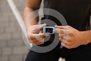 Man checking pulse with blood pressure monitor on finger after training outdoors, closeup. Space for text