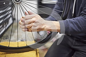 Man checking the tension of the spokes of a bicycle wheel in his bike workshop