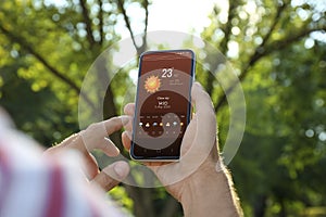 Man checking weather using app on smartphone outdoors, closeup. Data, sun and other illustrations on screen