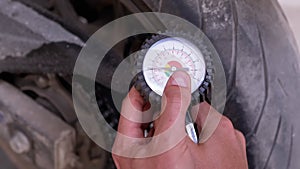 A Man Checks the Air Pressure in a Motorcycle Tire with a Pressure Gauge