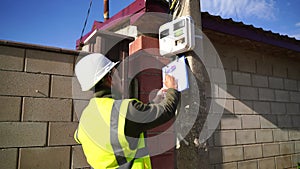 man checks the meter reading electricity in the cottage. An electrical engineer inspects a transformer box and makes