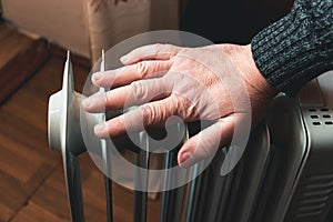 A man checks the temperature of an electric oil heater with his hand. In the off-season, central heating does not always work.