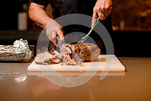 man chef accurate cuts cooked fried meat on white cutting board.