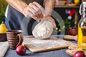 Man chef in a black apron kneads the dough with hands for Christmas baking. Joyful cooking for festive new year table