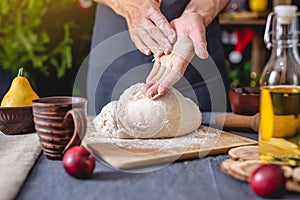 Man chef in a black apron kneads the dough with hands for Christmas baking. Joyful cooking for festive new year table