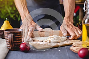 Man chef in a black apron kneads the dough with hands for Christmas baking. Joyful cooking for festive new year table