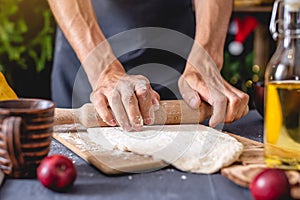 Man chef in a black apron kneads the dough with hands for Christmas baking. Joyful cooking for festive new year table