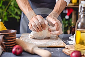 Man chef in a black apron kneads the dough with hands for Christmas baking. Joyful cooking for festive new year table