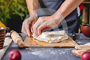 Man chef in a black apron kneads the dough with hands for Christmas baking. Joyful cooking for festive new year table