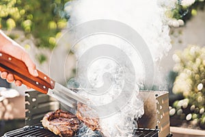Man chef grilling beef steak at barbecue dinner party outdoor - Close up male hand cooking meat on bbq for family in the garden