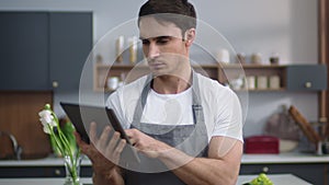 Man chef reading recipe on tablet at home kitchen. Man chef browsing internet.