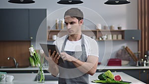 Man chef reading recipe on tablet at home kitchen. Man chef browsing internet.