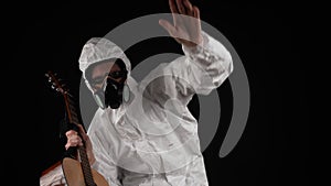 A man in a chemical protection suit dances with a guitar