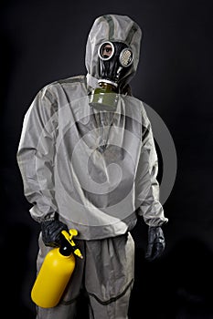 Man in a chemical protection suit and a gas mask. The guy is holding a yellow spray gun. Decontamination in special