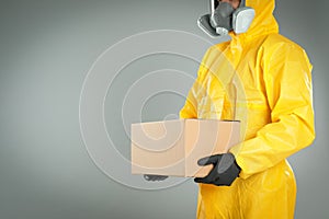 Man in chemical protective suit holding cardboard box on light grey background, closeup view. Prevention of