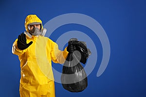 Man in chemical protective suit holding trash bag on background, space for text. Virus research