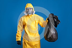 Man in chemical protective suit holding trash bag on background. Virus research